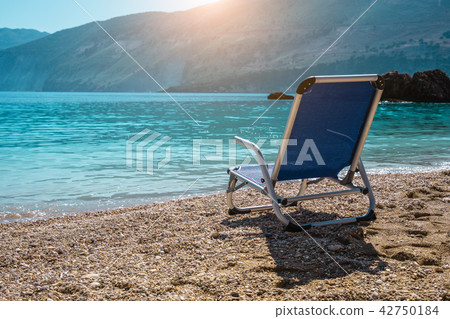 Beach chair from back on tranquil pebble beach. Amazing view to impressive rocks in the water 42750184
