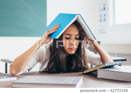 Tired girl studying at working table. Exhausted female student reading books. 42772336