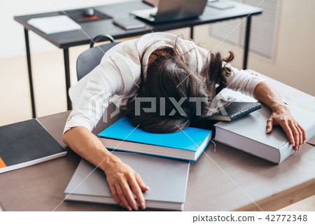 Tired female student sleeping on desk face and hands on books. 42772348