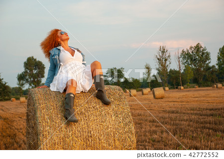 Red-haired woman posing on the field near a hay stack Red-haired woman posing on the field near a hay stack 42772552