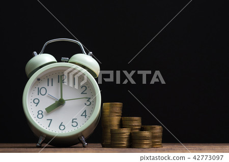 Alarm clock and coins stacks on working table Alarm clock and coins stacks on working table 42773097