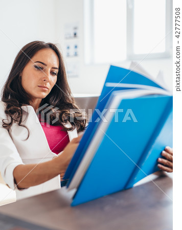 Young woman sitting by table and reading book 42777508