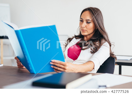 Young woman sitting by table and reading book 42777526