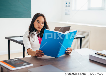 Young woman sitting by table and reading book. 42777527