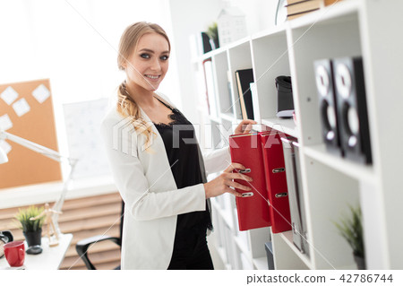 A young girl stands near a rack in the office and takes out a folder. A young girl stands near a rack in the office and takes out a folder. 42786744