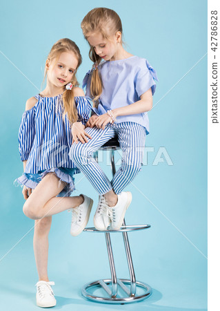 Girls twins in light blue clothes are posing near a bar stool on a blue background. Girls twins in light blue clothes are posing near a bar stool on a blue background. 42786828