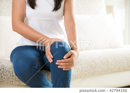 Woman sitting on sofa and feeling knee pain Woman sitting on sofa and feeling knee pain 42794188