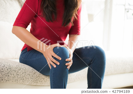 Woman sitting on sofa and feeling knee pain 42794189