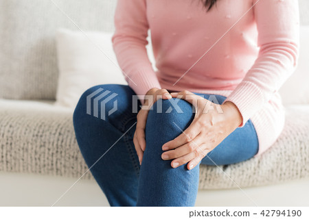 Woman sitting on sofa and feeling knee pain Woman sitting on sofa and feeling knee pain 42794190