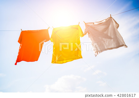 Photo of three T-shirts hanging on rope against blue sky background Photo of three T-shirts hanging on rope against blue sky background 42801617