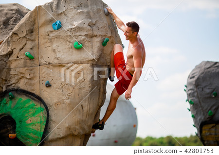 Photo of smiling guy in red shorts exercising on boulder for climbing against cloudy sky Photo of smiling guy in red shorts exercising on boulder for climbing against cloudy sky 42801753