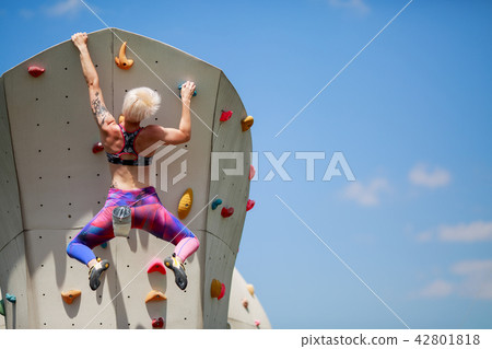 Photo from back of young athlete girl with short hairstyle climbing wall for rock against blue sky 42801818
