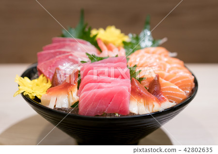Mixed sliced fish sashimi on ice in black bowl. 42802635