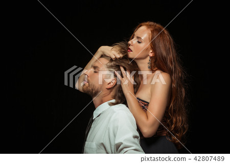 Real passion. Beautiful young loving couple bonding to each other while both standing against black 42807489