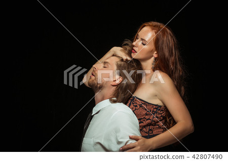 Real passion. Beautiful young loving couple bonding to each other while both standing against black 42807490