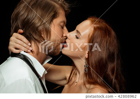 Real passion. Beautiful young loving couple bonding to each other while both standing against black Real passion. Beautiful young loving couple bonding to each other while both standing against black 42808962