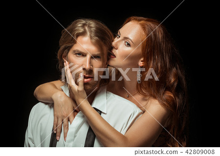 Real passion. Beautiful young loving couple bonding to each other while both standing against black Real passion. Beautiful young loving couple bonding to each other while both standing against black 42809008