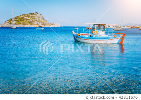Colorful greek fishing boat at the calm clear water on early summer morning. White rock at the 42811670