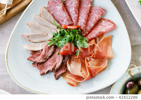 Food tray with delicious salami, pieces of sliced ham, sausage. Cutting sausage and cured meat on a 42812206