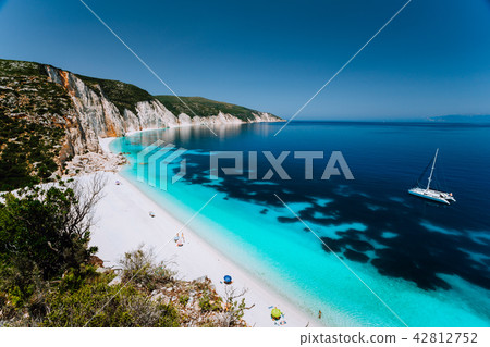 White catamaran yacht in clear blue sea water. Tourists on sandy beach near azure sea lagoon White catamaran yacht in clear blue sea water. Tourists on sandy beach near azure sea lagoon 42812752