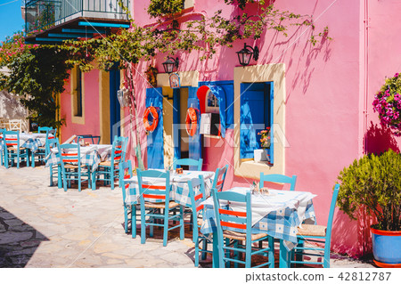 Traditional greek vivid lilac colored tavern on the narrow Mediterranean street on hot summer day Traditional greek vivid lilac colored tavern on the narrow Mediterranean street on hot summer day 42812787