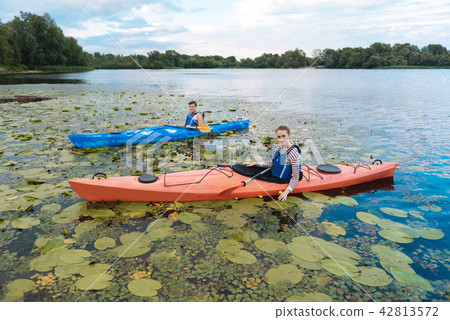 Young man and woman noticing many water lilies while kayaking Young man and woman noticing many water lilies while kayaking 42813572