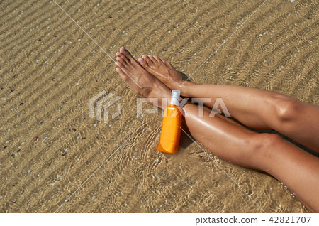 Beautiful, groomed woman's legs with a cream to protect sunburn from the sun in the summer on the 42821707