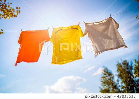 Photo of three T-shirts hanging on rope against blue sky background Photo of three T-shirts hanging on rope against blue sky background 42835535