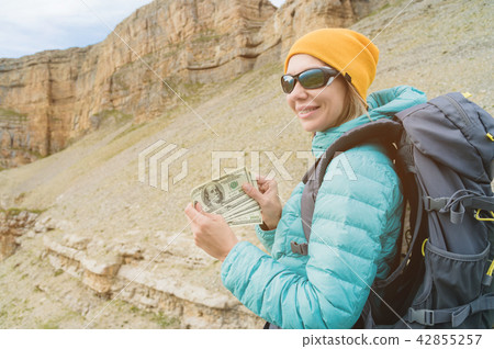 A traveler in a hat and sunglasses holds a hundred dollar bills in the hands of a fan against the A traveler in a hat and sunglasses holds a hundred dollar bills in the hands of a fan against the 42855257