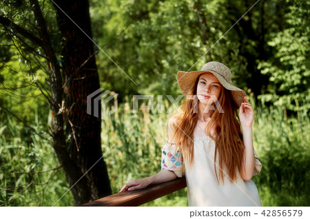A sophisticated red-haired girl in a simple linen dress, in a light wide-brimmed hat.Model look 42856579