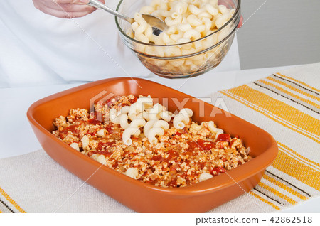 The cook prepares a meat casserole with pasta. 42862518