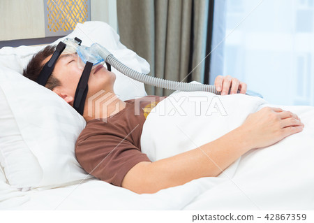 Asian man wearing CPAP mask, connecting to hose Asian man wearing CPAP mask, connecting to hose 42867359