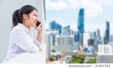 Happy young Asian woman on rooftop using her phone 42867362