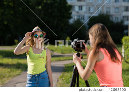 Two girlfriends schoolgirls in summer in the park records video on the camera. She is dressed in 42868500