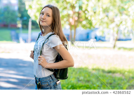 Girl schoolgirl in summer in the park. Happy smiling back on his backpack. Free space for text 42868582