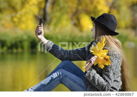 Girl in the hat sitting on pier and makes selfie Girl in the hat sitting on pier and makes selfie 42869867
