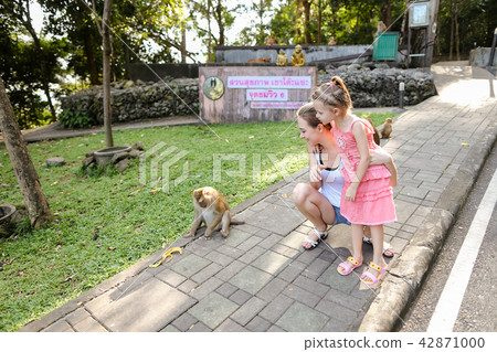 Young blonde mother with daughter standing near monkeys at zoo in Thailand. Young blonde mother with daughter standing near monkeys at zoo in Thailand. 42871000