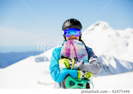 Photo of woman tourist in helmet looking into camera with snowboard in hands 42875446