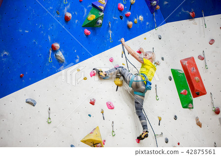 Photo from back of young sportswoman in yellow T-shirt scrambles on wall for climbing at workout 42875561