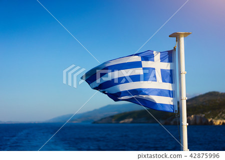 Flag of Greece waving over the see on cruise sheep in front of beautiful coastline 42875996