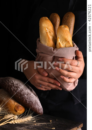 Baker woman holding rustic organic loaf of bread in hands - rural bakery. Natural light, moody still 42876221