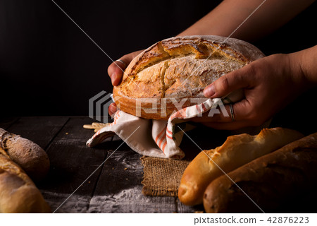 Baker woman holding rustic organic loaf of bread in hands - rural bakery. Natural light, moody still 42876223