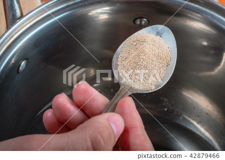 Female hand holds spoon with yeast over metal pan Female hand holds spoon with yeast over metal pan 42879466