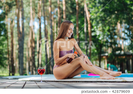 Woman using sun protection cream sitting near outside pool Woman using sun protection cream sitting near outside pool 42879609