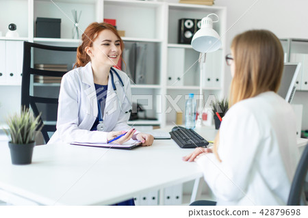 A beautiful young girl in a white robe is sitting at the desk in the office and communicating with A beautiful young girl in a white robe is sitting at the desk in the office and communicating with 42879698