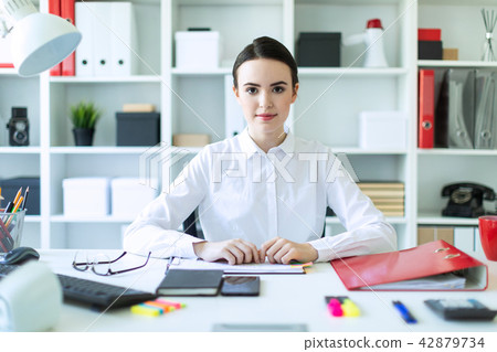 A young girl in the office sits at a table and holds a pen in her hands. 42879734