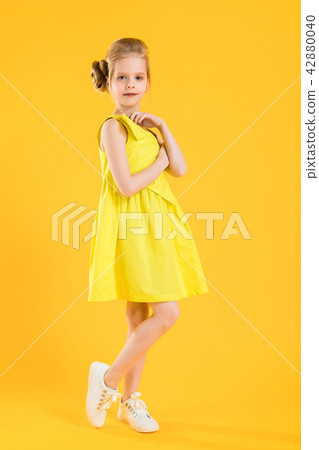 A blonde girl stands sideways on a yellow background. A blonde girl stands sideways on a yellow background. 42880040