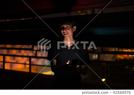 Portrait Of Asian Man Outdoors At Night In Parking Lot Using Mobile Phone 42888976