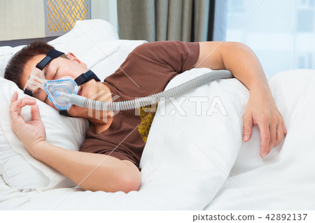 Asian man wearing CPAP mask, connecting to hose 42892137