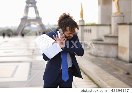 Jocund mulatto guy raving near Eiffel Tower and calling friend b Jocund mulatto guy raving near Eiffel Tower and calling friend b 42894127